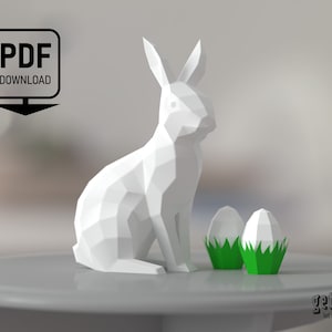 May include: White papercraft bunny rabbit sitting on a grey surface with two green papercraft Easter eggs beside it.  PDF DOWNLOAD text is in the top left corner of the image.
