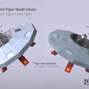 May include: A gray, round, flying saucer with red landing gear. The saucer has a small, round window in the top and a small, round opening in the bottom. The text "Mini Figur bleibt sitzen" and "mini figure sits tight" is printed in black on a white background above the saucer. The text "* Figur nicht enthalten" and "mini figure not included" is printed in black on a white background below the saucer. The text "getide let's make it" is printed in black on a white background below the saucer.