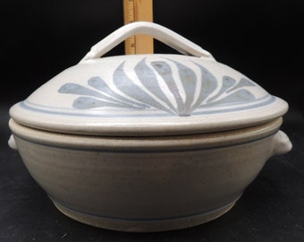 May include: A white ceramic casserole dish with a lid. The lid features a blue and white floral design. The dish has two small handles on the sides.