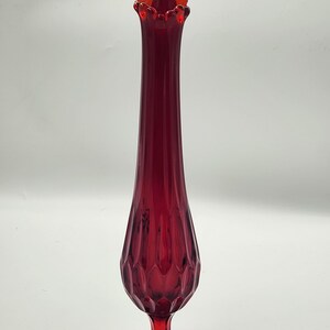 May include: A tall, ruby red glass vase with a flared, ruffled rim. The vase has a slender, elongated body with a textured, diamond-like pattern. It stands on a round base, showcasing a classic, elegant design.