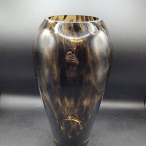 May include: A black and gold glass vase with a mottled pattern. The vase has a round base and a narrow neck.