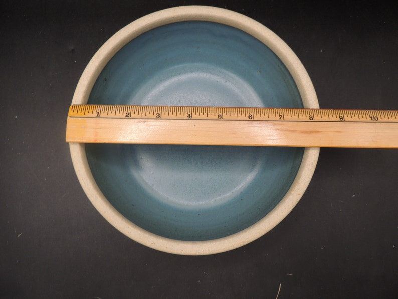 May include: A light blue ceramic bowl with a white rim. The bowl is approximately 10 inches in diameter.