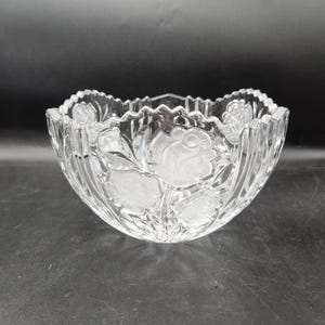 May include: A clear glass bowl with a scalloped edge and etched rose designs. The bowl features vertical ribbed sides and a frosted floral pattern. The bowl is suitable for serving or display.
