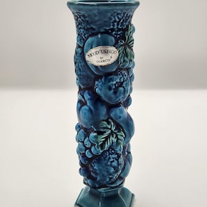 Puede incluir: Un jarrón de cerámica color turquesa con superficie texturizada y base hexagonal. El jarrón está adornado con diseños de frutas y hojas en relieve. Una etiqueta dice "MOOD INDIGO by INARCO".