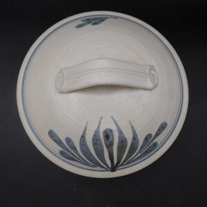 May include: White ceramic bowl with a blue and white floral design and a handle. The bowl has a simple, elegant design.