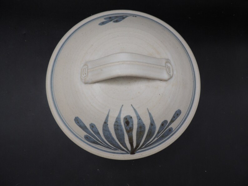 May include: White ceramic bowl with a blue and white floral design and a handle. The bowl has a simple, elegant design.