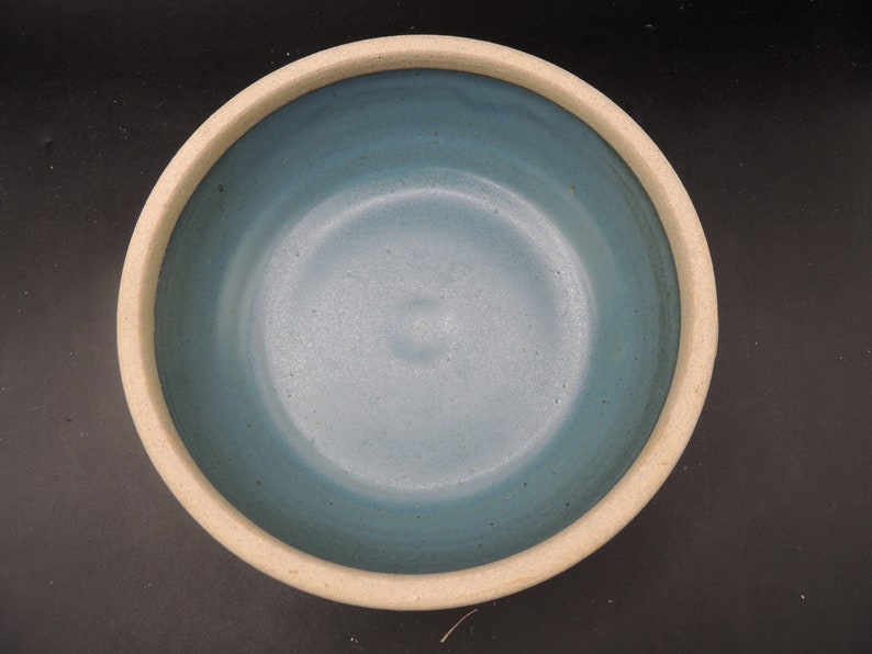 May include: A light blue ceramic bowl with a white rim. The bowl is empty and has a smooth, glossy finish.
