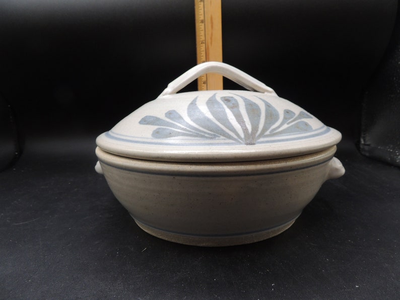 May include: A white ceramic casserole dish with a lid. The lid features a blue and white floral design. The dish has two small handles on the sides.