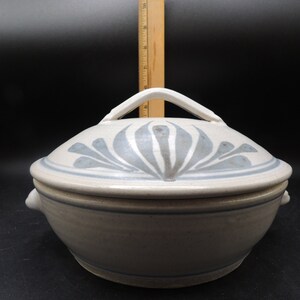May include: A white ceramic casserole dish with a lid. The lid features a blue and white floral design and a white handle. The dish has two small handles on the sides.