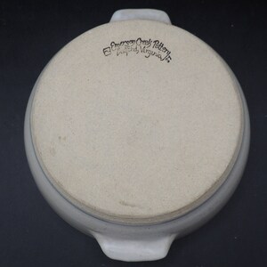 May include: A white ceramic baking dish with two handles. The bottom of the dish has a blue rim and the words "Emerson Creek Pottery, Bluford, Virginia" in black.