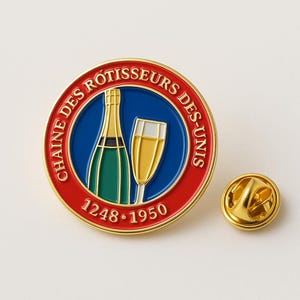 Puede incluir: Un pin redondo dorado con borde rojo y centro azul. El pin presenta una botella de champán verde y dorada y una copa de champán. También es visible el texto "CHAINE DES ROTISSEURS DES-UNIS" y los números "1248-1950". Se incluye un pasador dorado separado.