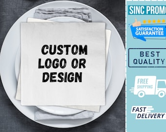 May include: White cloth napkin with black text that reads "CUSTOM LOGO OR DESIGN" on a white plate. The napkin is folded in half and placed on top of a white plate. The plate is on a gray surface.