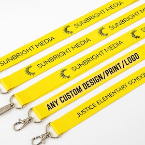 May include: Yellow lanyards with silver metal clasps. The lanyards have black text that reads "SUNBRIGHT MEDIA" and a sun logo. One lanyard reads "ANY CUSTOM DESIGN/PRINT/LOGO" and another reads "JUSTICE ELEMENTARY SCHOOL".