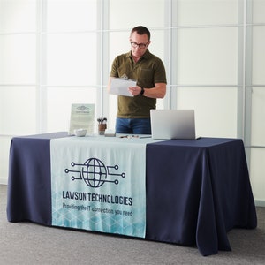 Op de afbeelding: Een donkerblauwe tafelkleed met een witte en blauwe bedrukte tafelrunner. De tafelrunner heeft een wereldbol met een print van een printplaat en de tekst "LAWSON TECHNOLOGIES Providing the IT connection you need".