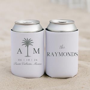 Op de afbeelding: Twee witte blikjeskoelers met zilveren deksels, op zand. Eén heeft een palmboomafbeelding met initialen en een datum, de andere leest "the RAYMONDS". Perfect voor een strandbruiloft of evenement.