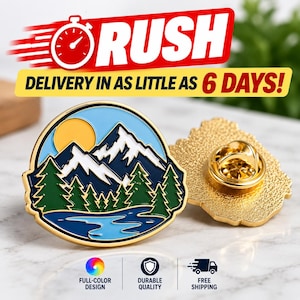 May include: A round metal enamel pin featuring a landscape design with a yellow sun, white snow-capped dark blue mountains, green pine trees, and a light blue lake. The back of the pin is gold-toned with a metal clutch fastener attached.