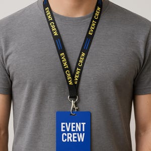 May include: Black lanyard with the text "EVENT CREW" in yellow. The lanyard has blue stripes and a blue rectangular badge with the same text in white. A silver clasp is attached to the badge.