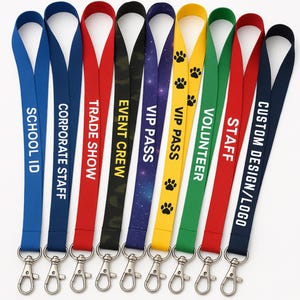 May include: A collection of lanyards in various colors, each with a different text. The lanyards include the following text: "SCHOOL ID", "CORPORATE STAFF", "TRADE SHOW", "EVENT CREW", "VIP PASS", "VOLUNTEER", "STAFF", and "CUSTOM DESIGN/LOGO". Each lanyard has a metal clasp.