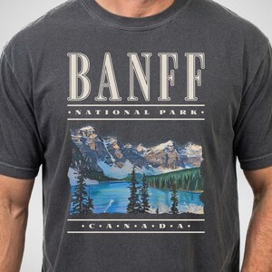 A model wears a Pepper Comfort Colors t-shirt with a retro nineties design featuring a graphic of Moraine Lake and the text, "Banff National Park Canada" in off-white vintage style text.