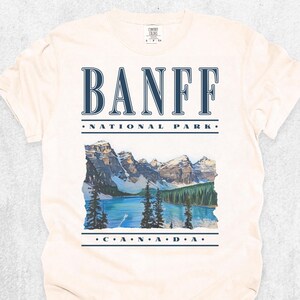 An Ivory Comfort Colors t-shirt with vintage text reading "Banff National Park" and "CANADA," with a graphic illustration of Moraine Lake.