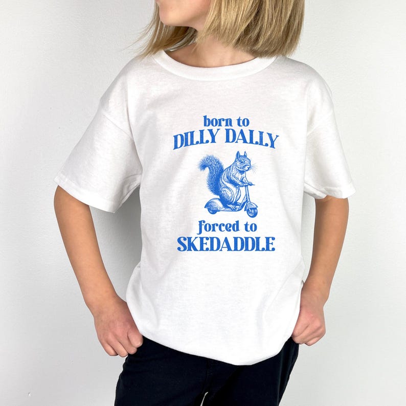 May include: White t-shirt with blue text that reads "born to dilly dally forced to skedaddle". A blue illustration of a squirrel riding a scooter is above the text.