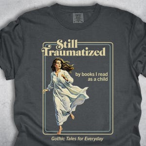 May include: Dark gray t-shirt with the text "Still Traumatized" and "by books I read as a child." A vintage illustration of a woman in a white nightgown running is featured. The phrase "Gothic Tales for Everyday" is at the bottom.