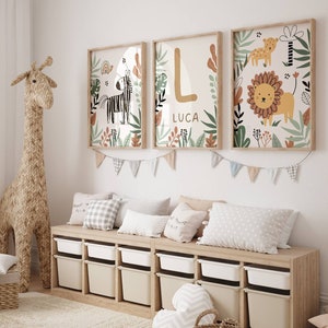 May include: A nursery room with a white wall, a wooden storage bench with white bins, and three framed prints with jungle animal illustrations. The prints feature a zebra, a lion, and the letter L with the name Luca below it. A stuffed giraffe stands next to the bench.
