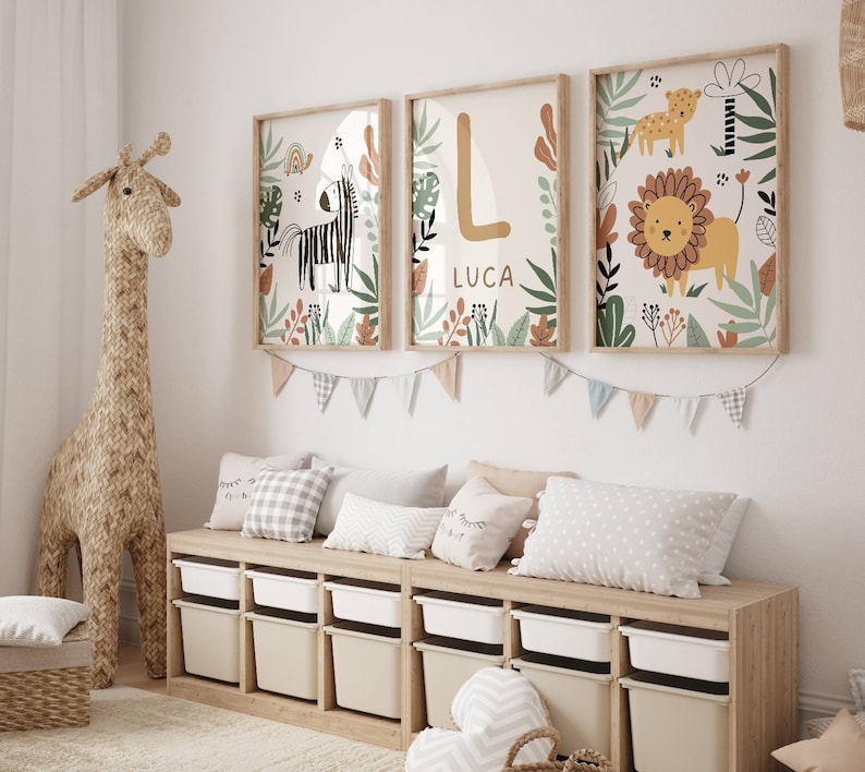 May include: A nursery room with a white wall, a wooden storage bench with white bins, and three framed prints with jungle animal illustrations. The prints feature a zebra, a lion, and the letter L with the name Luca below it. A stuffed giraffe stands next to the bench.