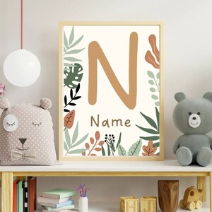 May include: A beige and brown framed print with a large orange letter N surrounded by green and brown leaves. The text "Name" is below the letter.