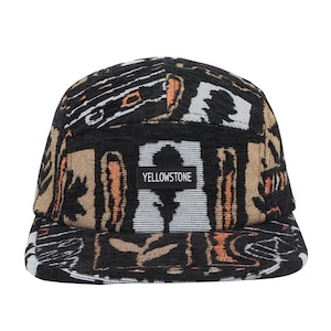 May include: A five-panel cap with a patterned design in black, tan, and orange. The cap features the word "YELLOWSTONE" on a rectangular patch. The brim is flat, and the cap is made of a woven fabric.