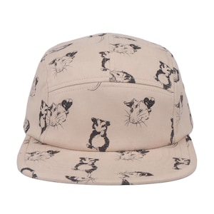 May include: A five-panel cap in a light beige colour featuring an all-over black ink-style print of opossums in various poses, including close-up portraits and full-body illustrations, with a flat brim and a structured crown design.