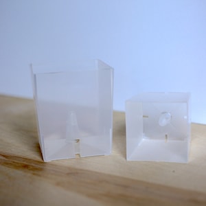 May include: Two clear plastic square containers with a small hole in the bottom of each.