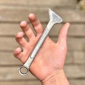 May include: A silver wrench with a unique triangular head and a circular opening at the base. The wrench is made of drop-forged steel and is designed for mechanical tasks. The text "DROP FORGED STEEL TAIWAN" is printed on the wrench.