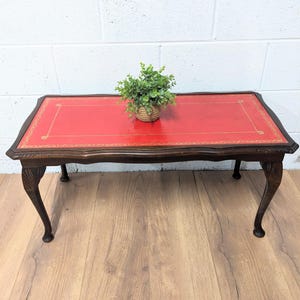 May include: A red leather-topped coffee table with a carved wooden frame and four cabriole legs. A small potted plant sits on the table.