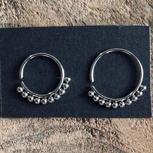 May include: Two silver hoop earrings with a row of small silver beads around the bottom of each hoop.