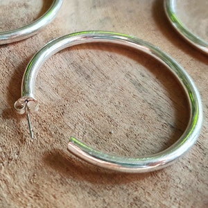 Puede incluir: Cuatro pendientes de aro plateados de diferentes tamaños sobre una superficie de madera.