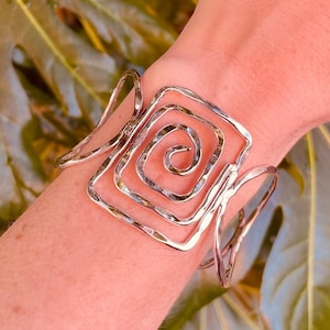 Op de afbeelding: Een zilveren armband met een geometrisch ontwerp. De armband is gemaakt van gedraaid draad en heeft een gehamerde afwerking.