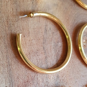 May include: Set of four gold hoop earrings of varying sizes. The earrings are made of a thick, round metal and have a polished finish.