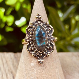 Pode incluir: Um anel de ouro com uma grande pedra de labradorita ovalada engastada em um design detalhado e ornamentado.