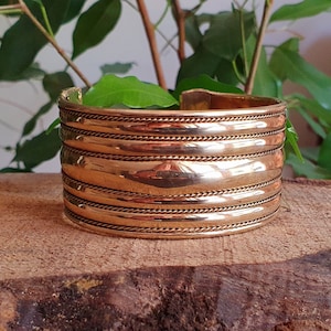 May include: A wide, gold-toned metal cuff bracelet with a textured, ridged design. The bracelet has five raised bands with a subtle rope-like detail.