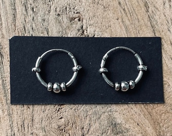 May include: A pair of silver hoop earrings with small beads around the hoop.