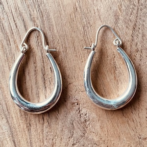 May include: A pair of silver hoop earrings with a rounded, oval shape. The earrings are simple and elegant.