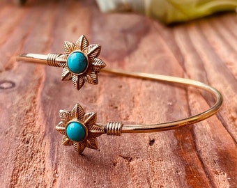 May include: A gold bangle bracelet with two turquoise flower accents. The bracelet is open and has a simple design.