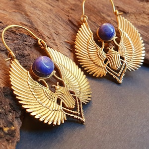 May include: Gold hoop earrings featuring a blue gemstone and a detailed design of a winged creature.