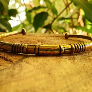Puede incluir: Un brazalete de metal dorado con un diseño simple y texturizado. El brazalete está abierto y tiene una forma ligeramente curvada.