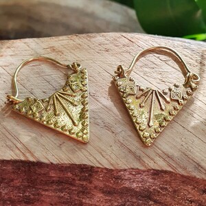 May include: A pair of gold triangle hoop earrings with intricate geometric designs. The earrings are made of metal and have a polished finish.