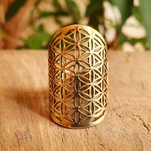 Puede incluir: Un anillo de color dorado con un diseño geométrico de la flor de la vida. El anillo es ancho y tiene una forma redondeada.