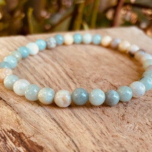 May include: A light blue and white beaded bracelet made of natural stones. The bracelet is made of round beads and is strung on a clear elastic cord.