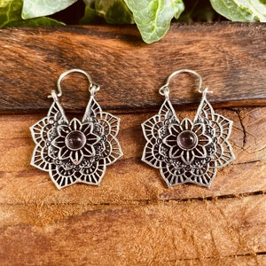 Può includere: Un paio di orecchini a cerchio d'argento con un design a mandala e una pietra preziosa viola al centro di ogni orecchino.