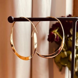 May include: A pair of gold hoop earrings with a unique curved design. The earrings are displayed on a black stand.
